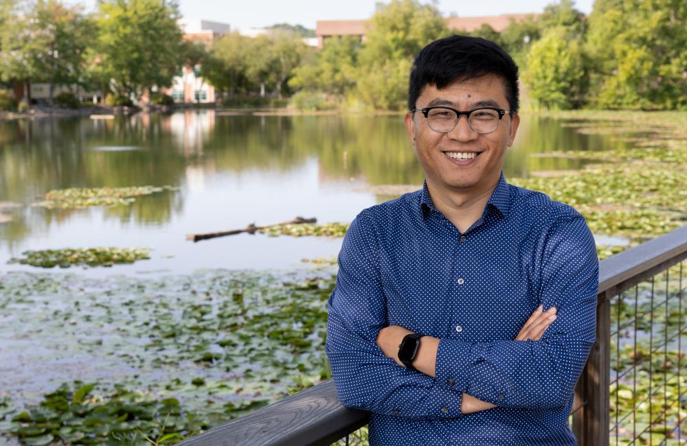 Daryl Yang standing on a bridge overlooking a pond covered in water lillies 