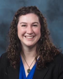 Photograph of Mary Barnacz- brown curly hair, brown eyes, wearing a blue top with black blazer